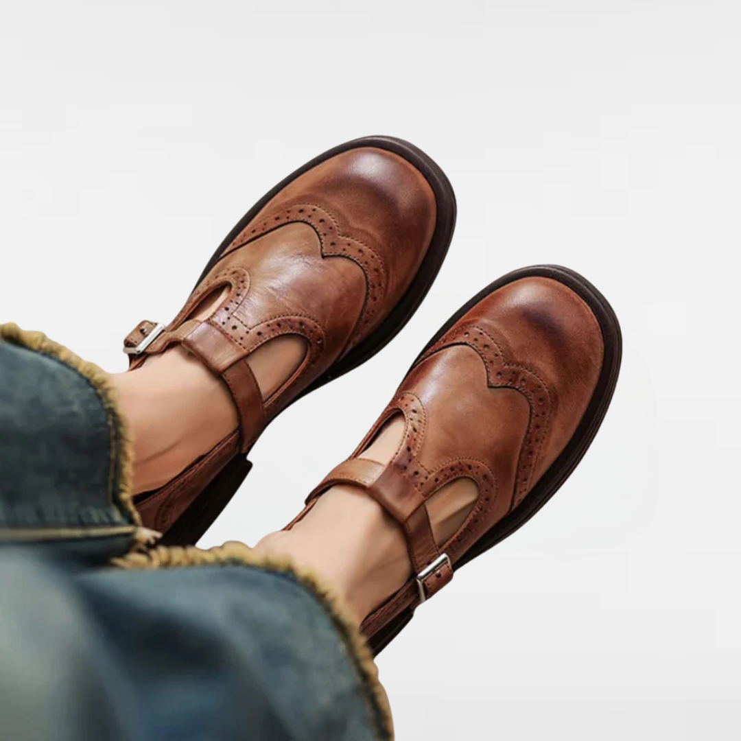 Brown leather Mary Jane flats with brogue perforations and T-strap buckle.