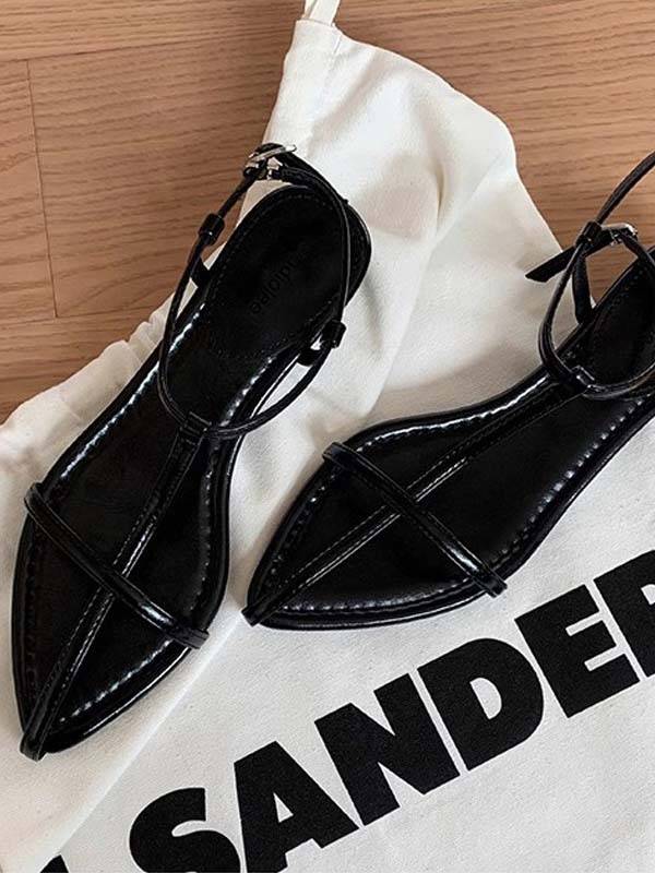Black faux leather T-strap flat sandals with pointed toe and adjustable ankle strap