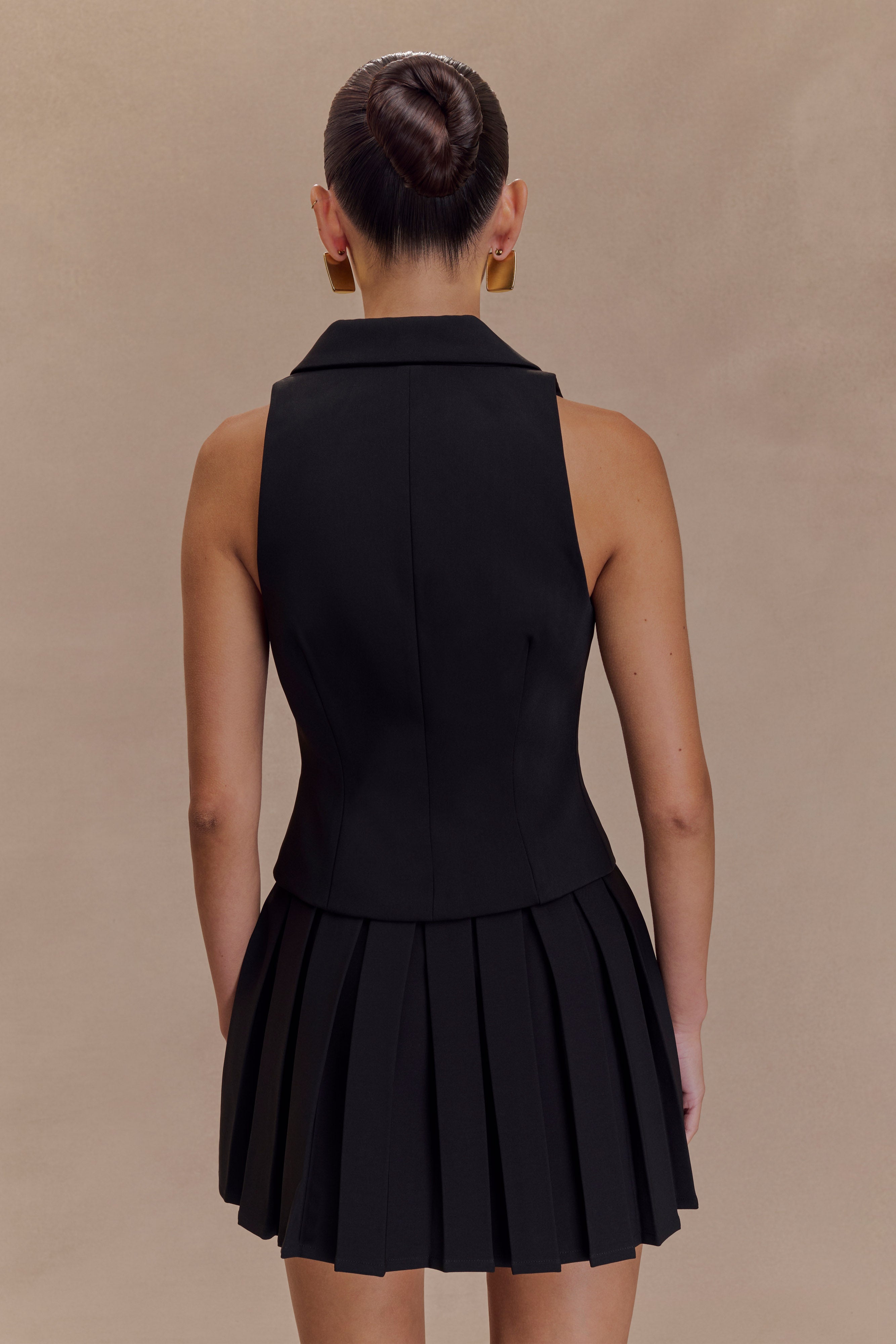 Black pleated mini skirt with structured waistband, belt loops, shown from behind