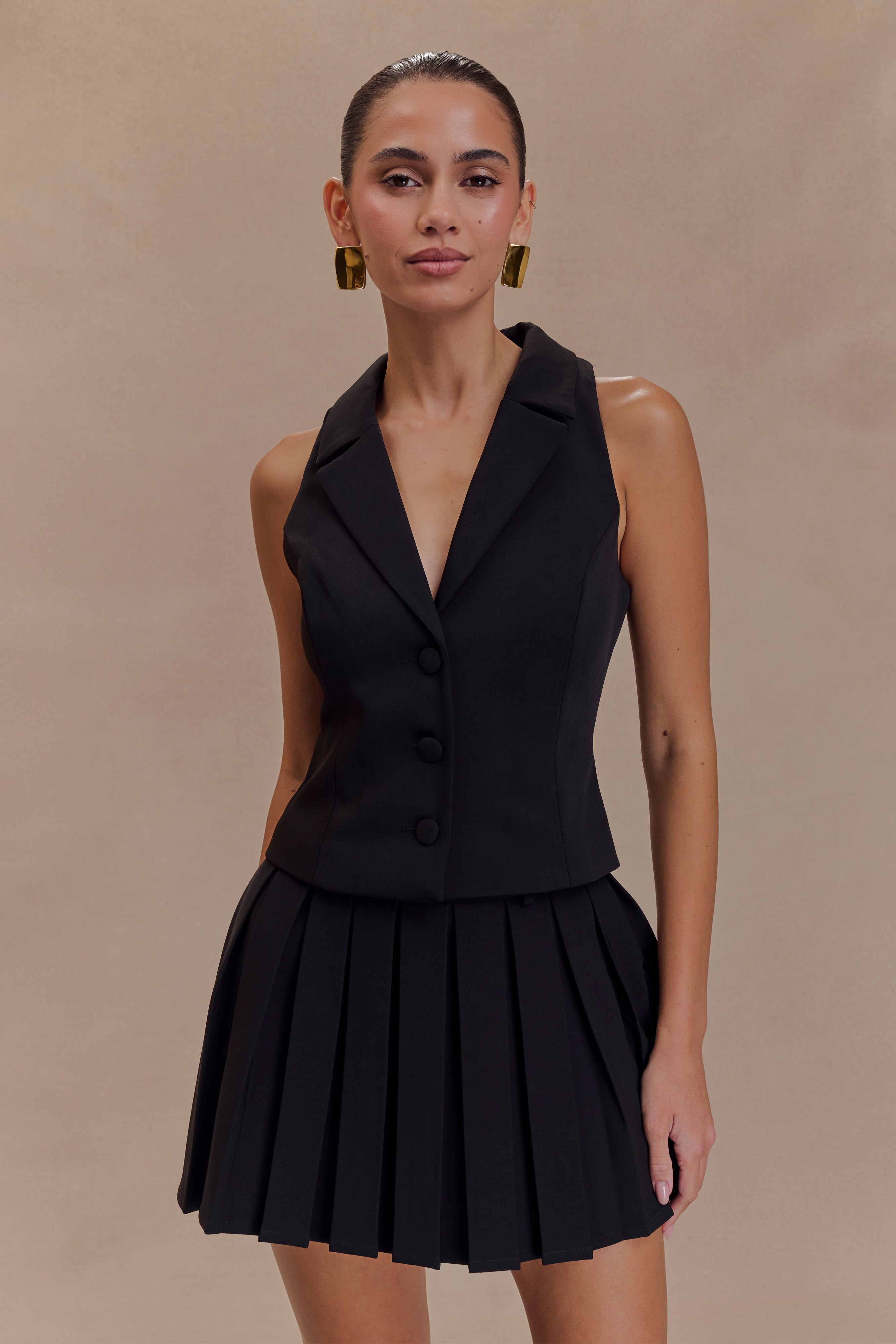 Black pleated mini skirt with structured waistband and belt loops, worn with vest