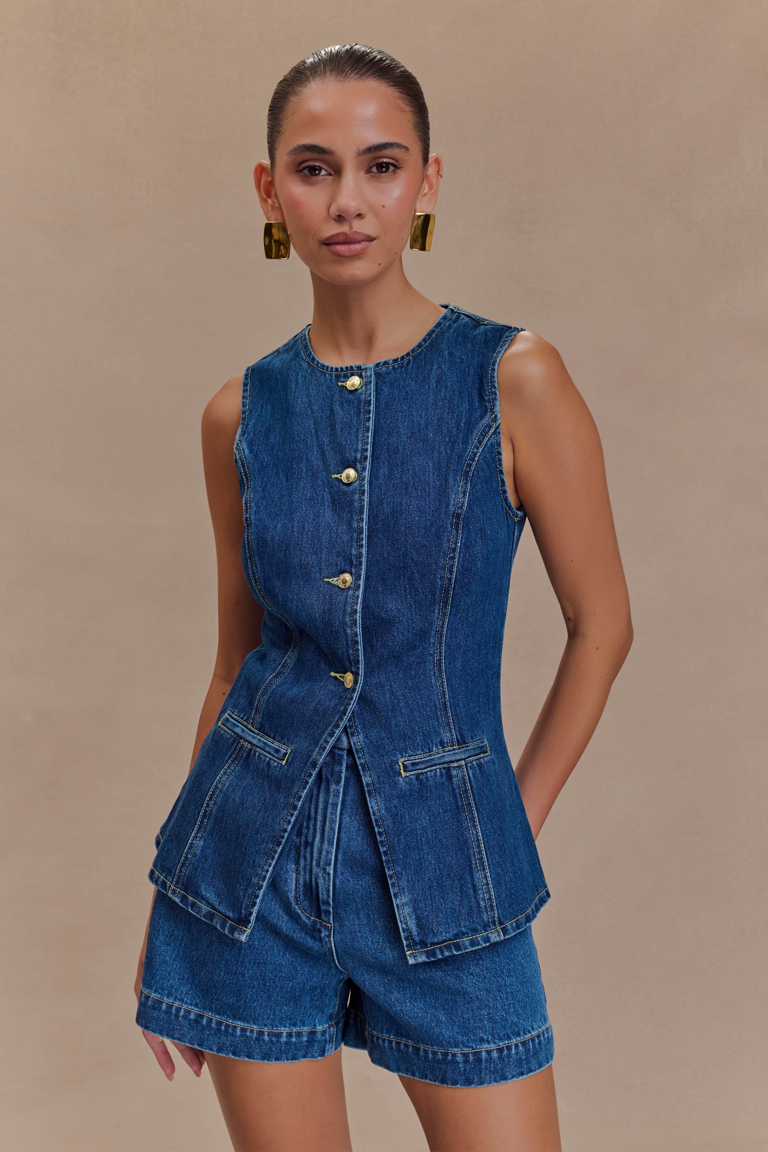 Blue denim sleeveless vest with gold buttons and asymmetrical flap pockets