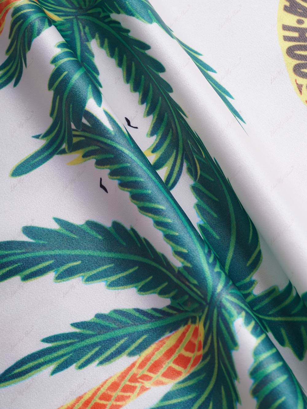 Satin fabric close-up with teal green palm leaf pattern on white base