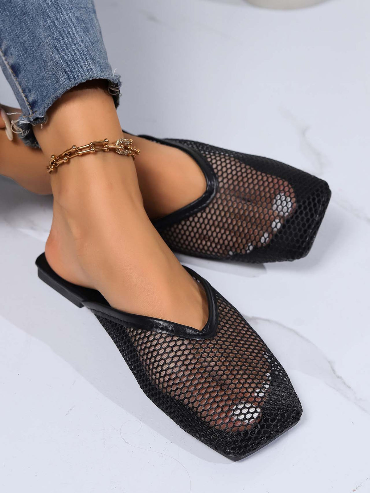Black mesh mules on feet, flat slip-on with square toe and breathable cutout front.