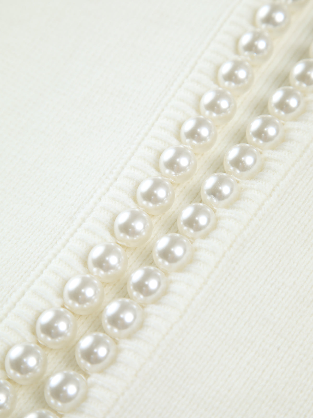 Close-up of cream knit cardigan with row of pearl-look buttons along trim