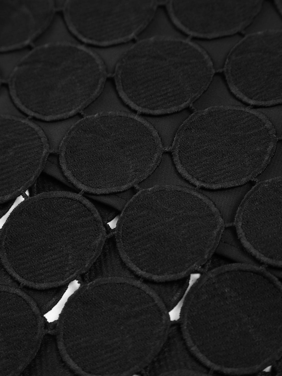 Black mesh fabric with stacked circular disc appliques, close-up texture