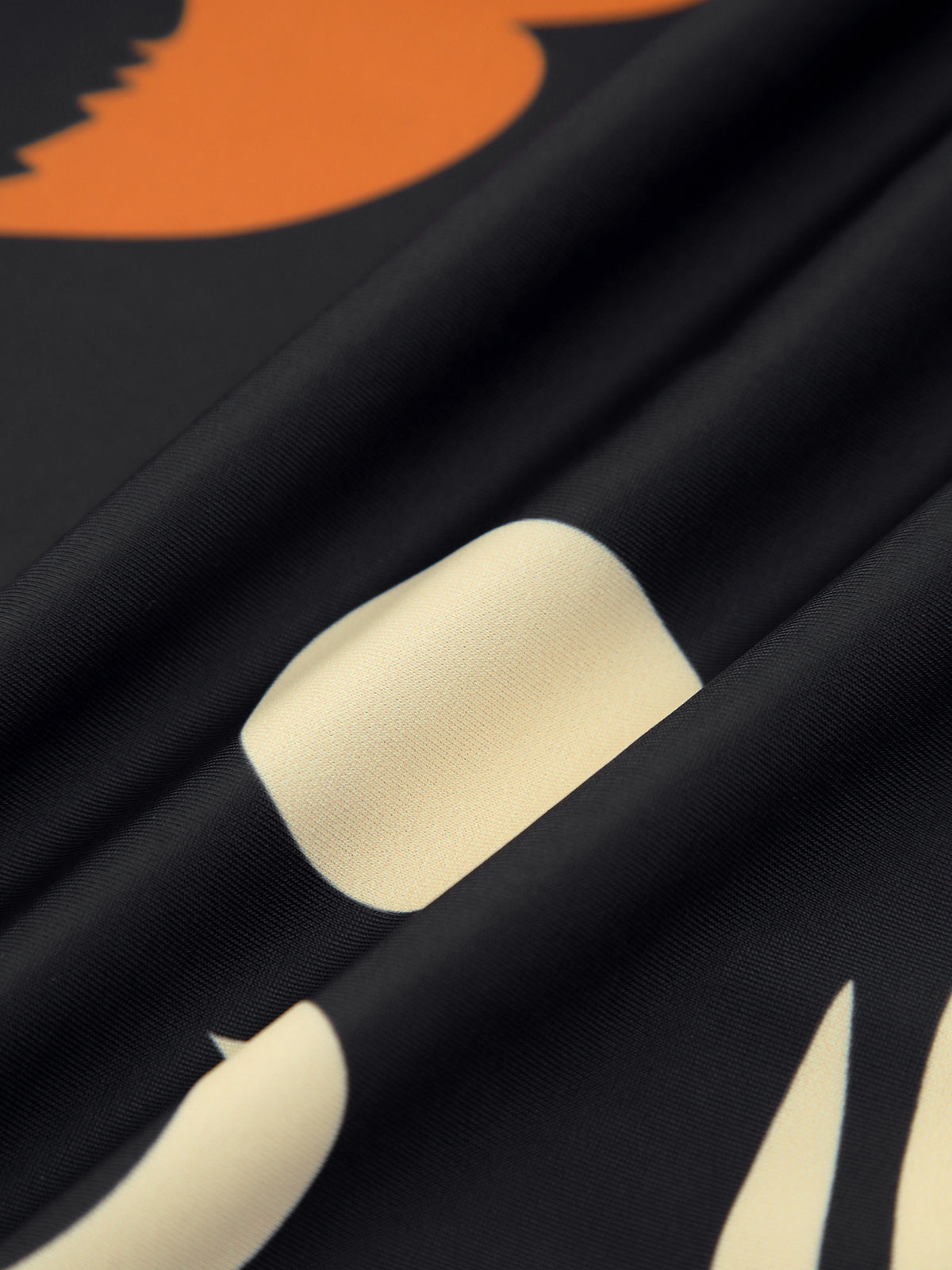 Stretch nylon fabric close-up in black with orange print and cream design accents