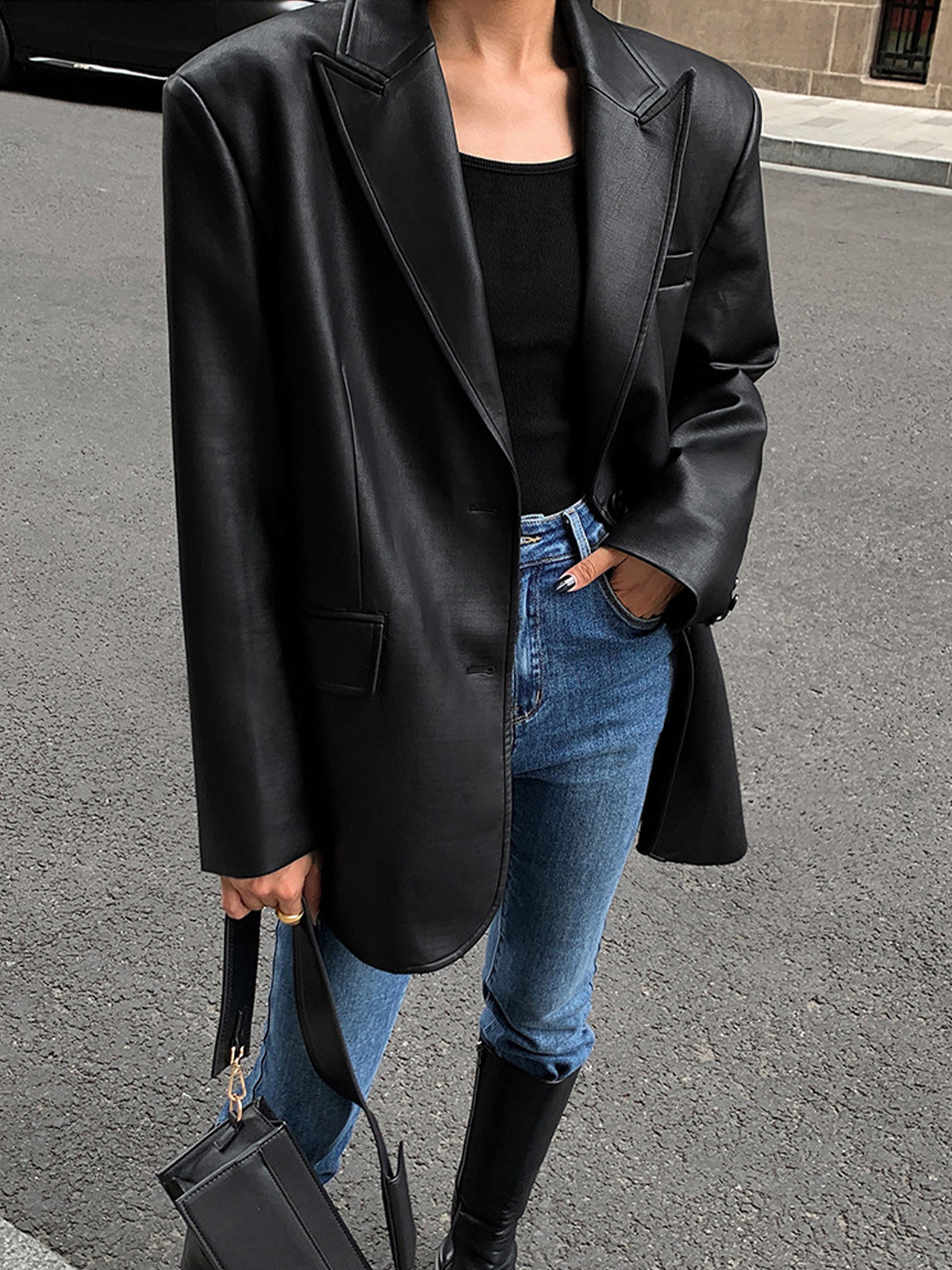 Black faux leather blazer with wide lapels and flap pockets, side-front view