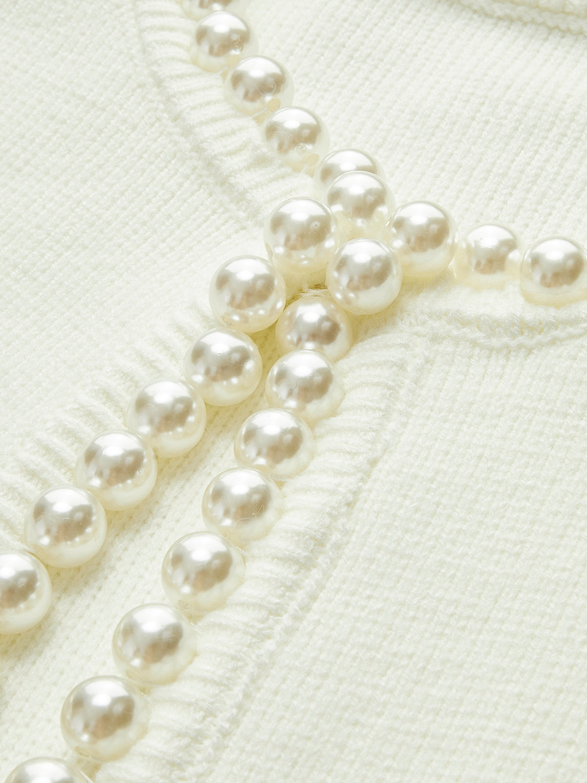 Close-up of pearl-look trim buttons on cream knit cardigan front
