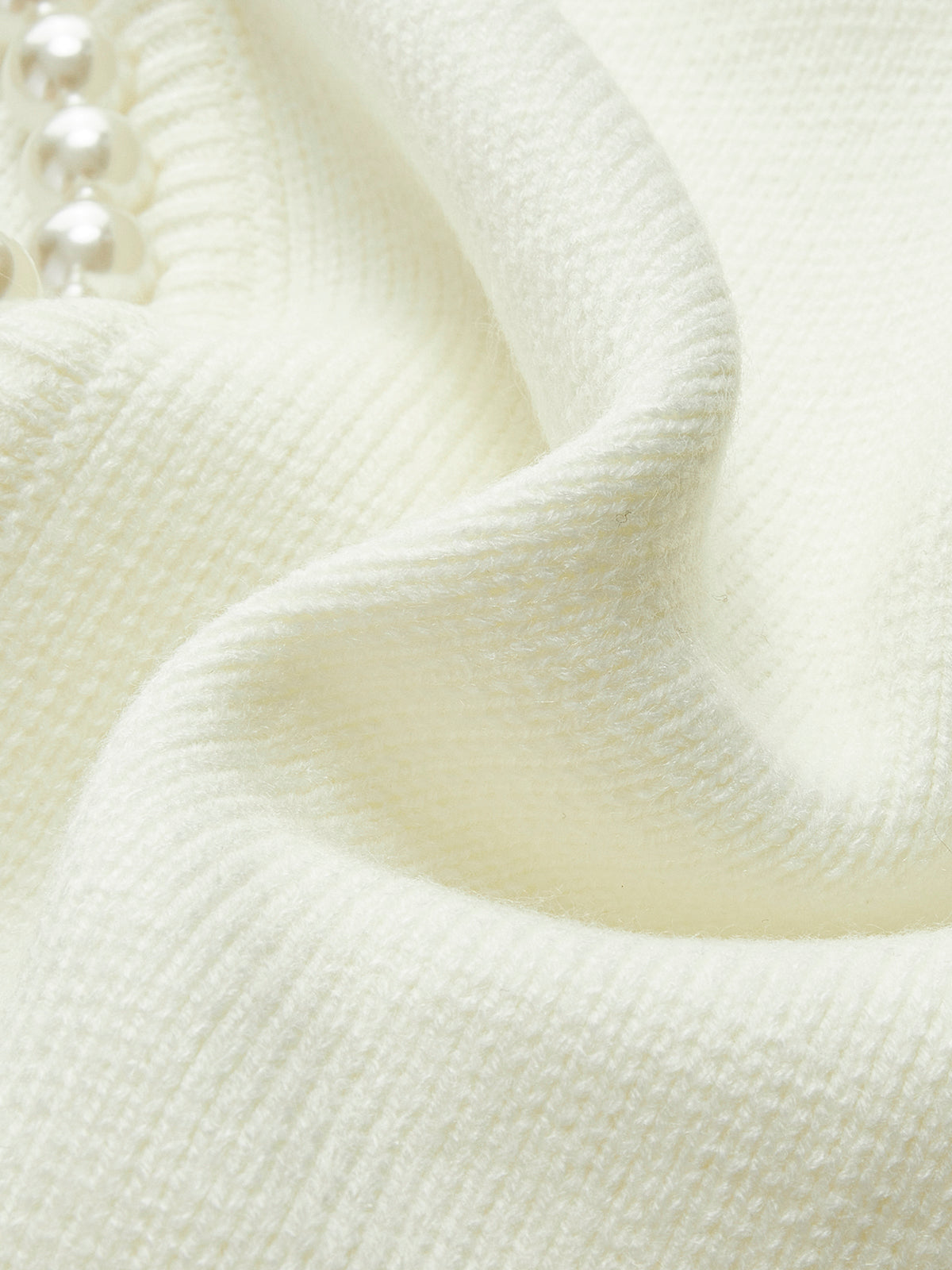 Close-up of cream knit cardigan sleeve fabric with soft ribbed texture