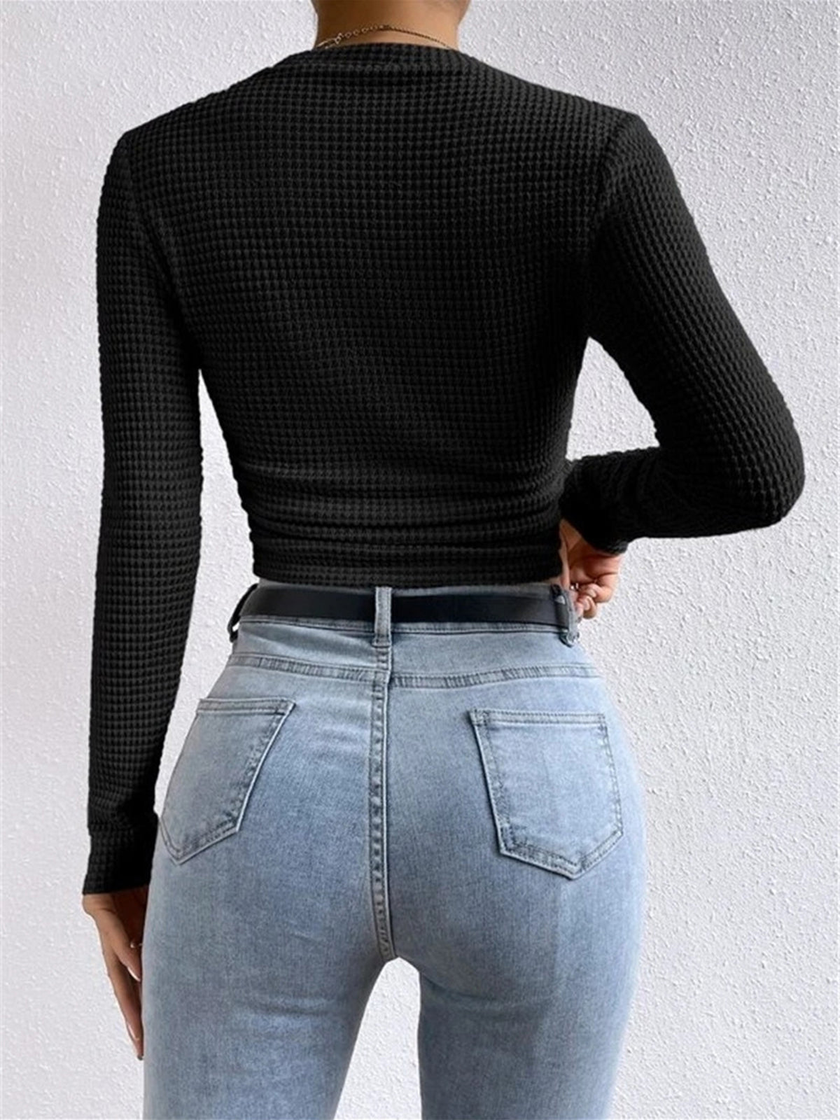 Back view of black waffle-knit long-sleeve slim crop top with ruched hem.