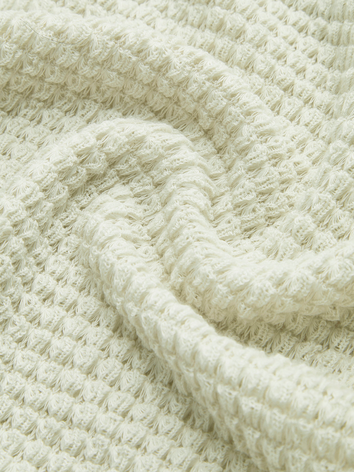 Close-up of light cream waffle-knit fabric with textured grid pattern.