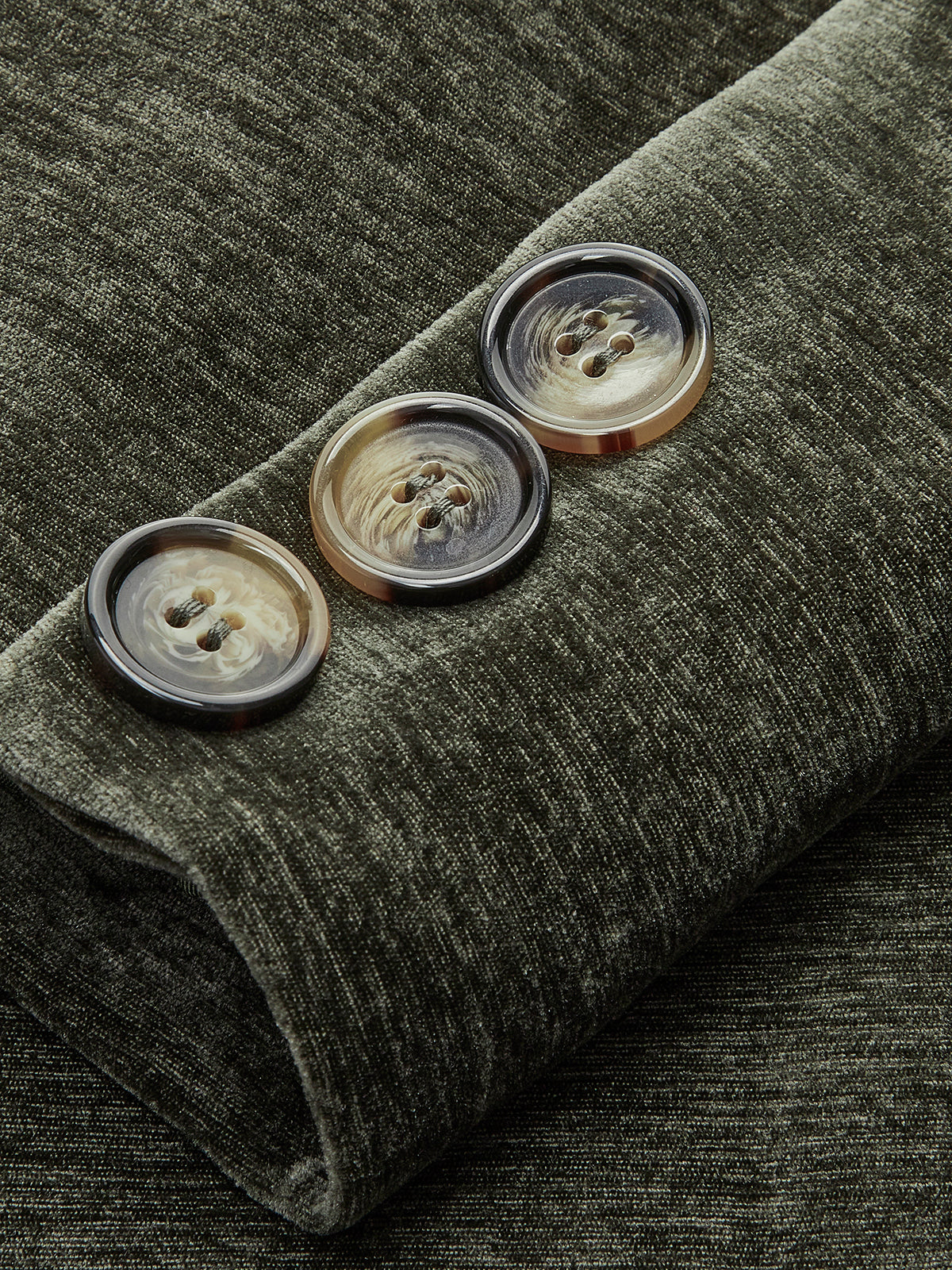 Close-up of dark green velvet blazer cuff with four gold-tone buttons