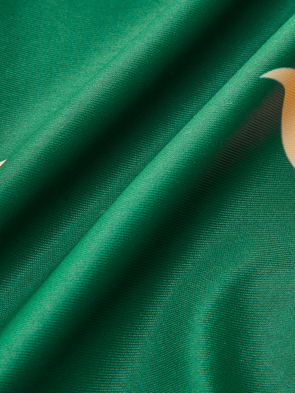 Dark green one-piece swimsuit fabric close-up with printed cream crescent and bird shapes