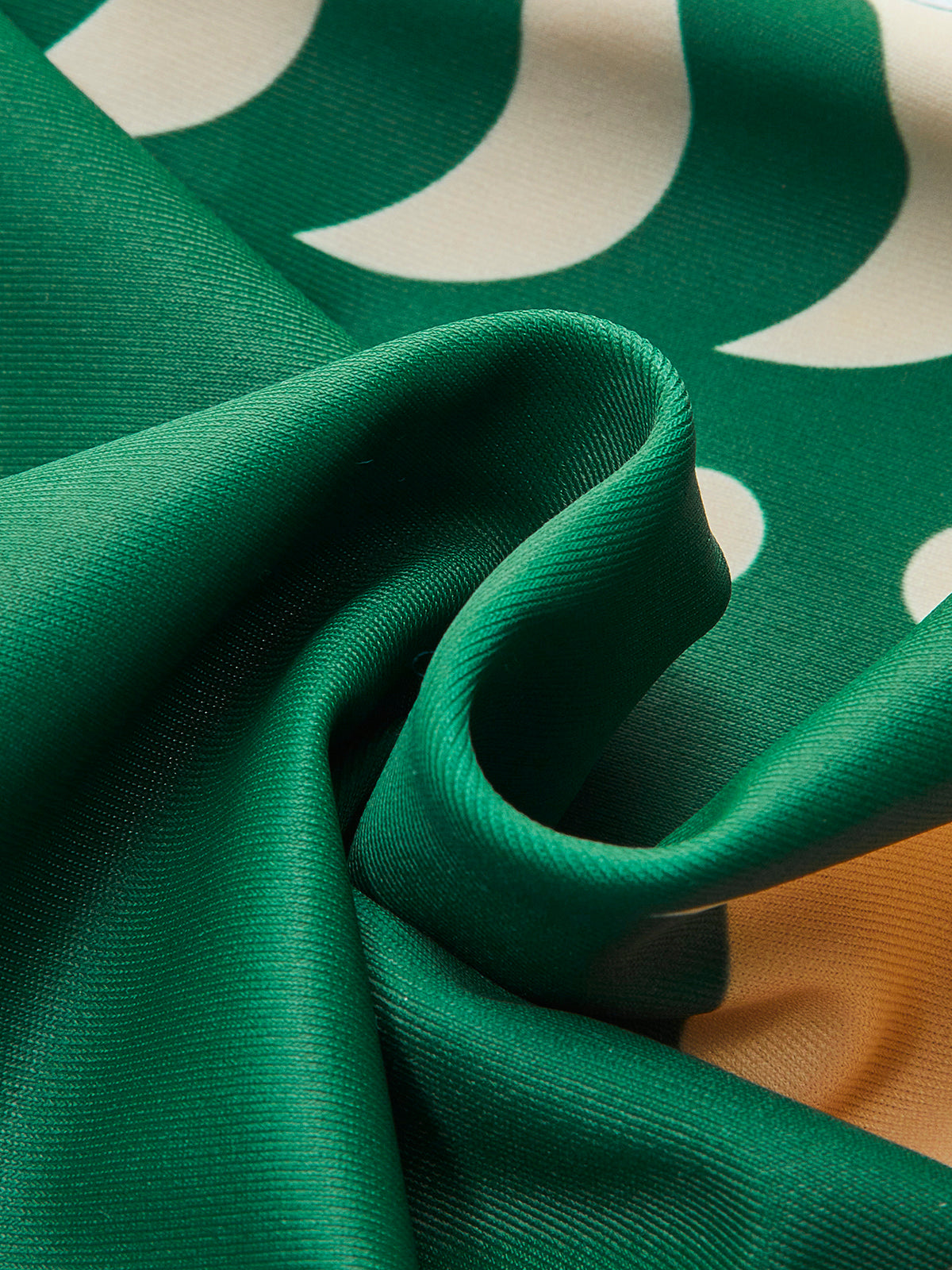 Dark green swim fabric close-up with draped folds and cream crescent print