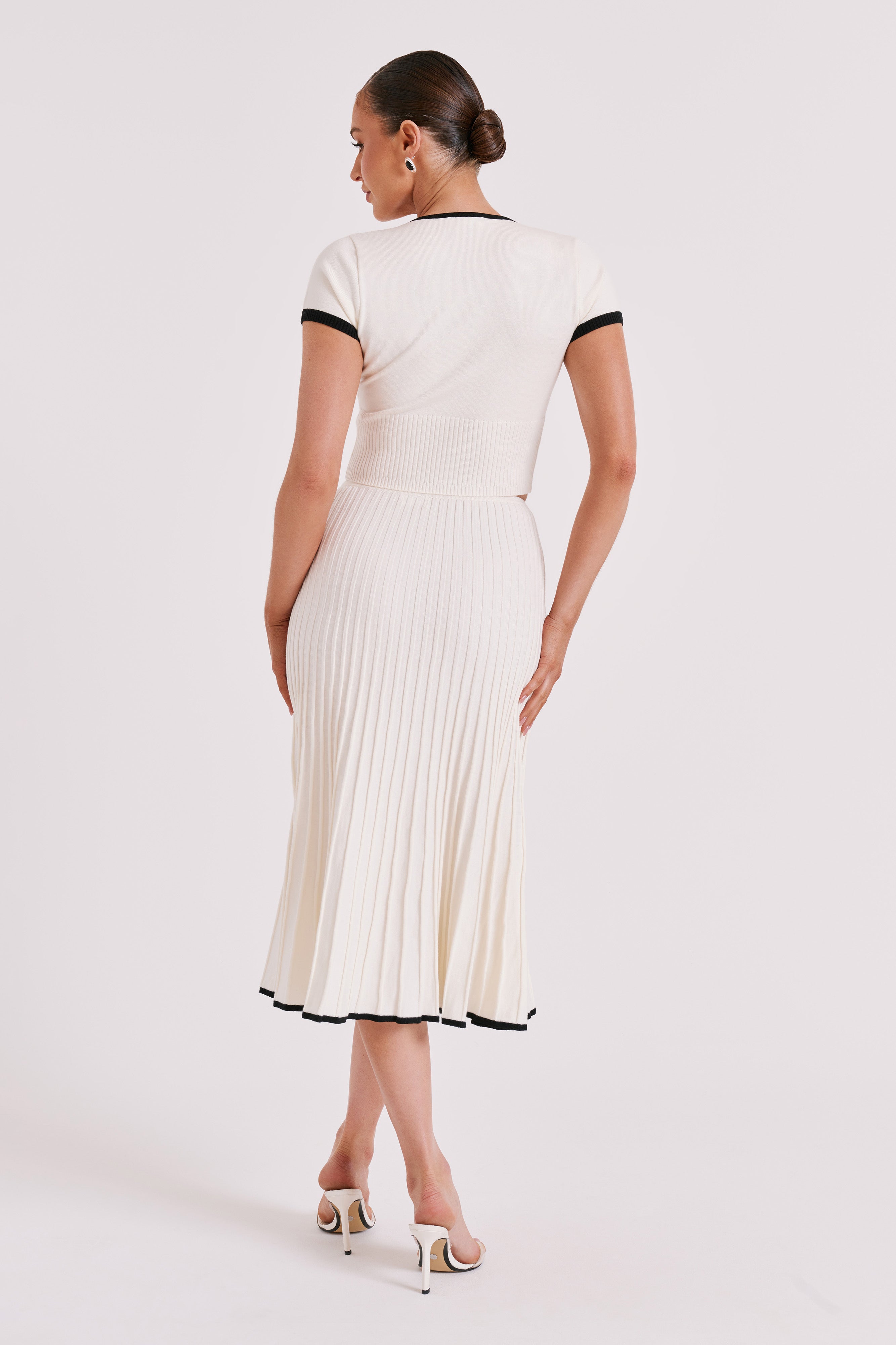 Back view of white pleated midi skirt with ribbed crop top and black-trim sleeve edges.