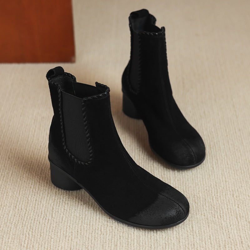 Black suede Chelsea ankle boots with round toe and chunky low heel, on floor