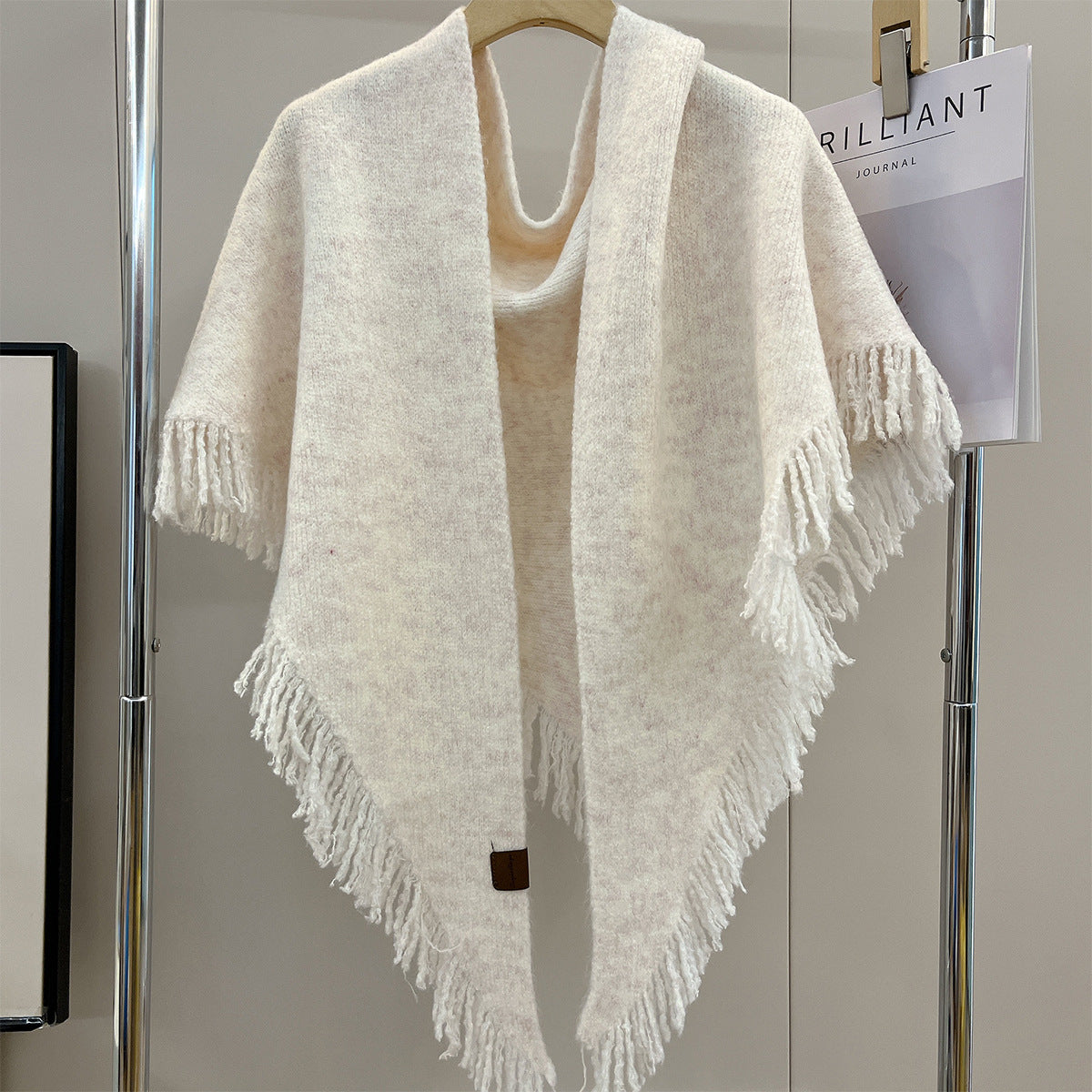 Cream triangle shawl with short tassel fringe along the edges, on hanger