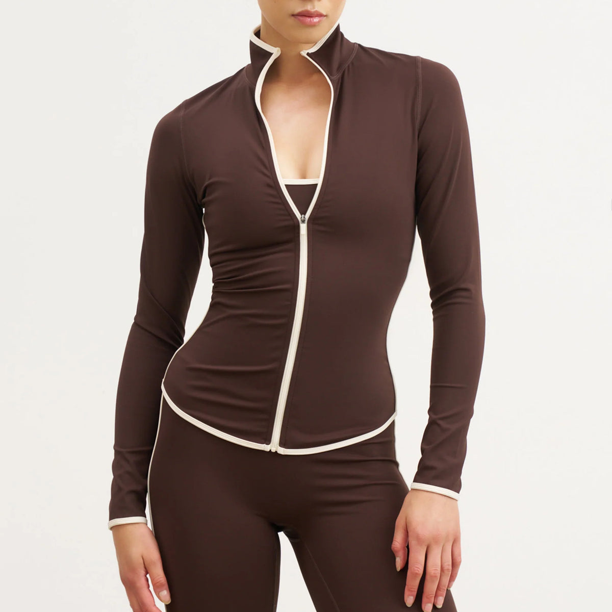 Brown fitted yoga jacket with white trim and partly open zipper