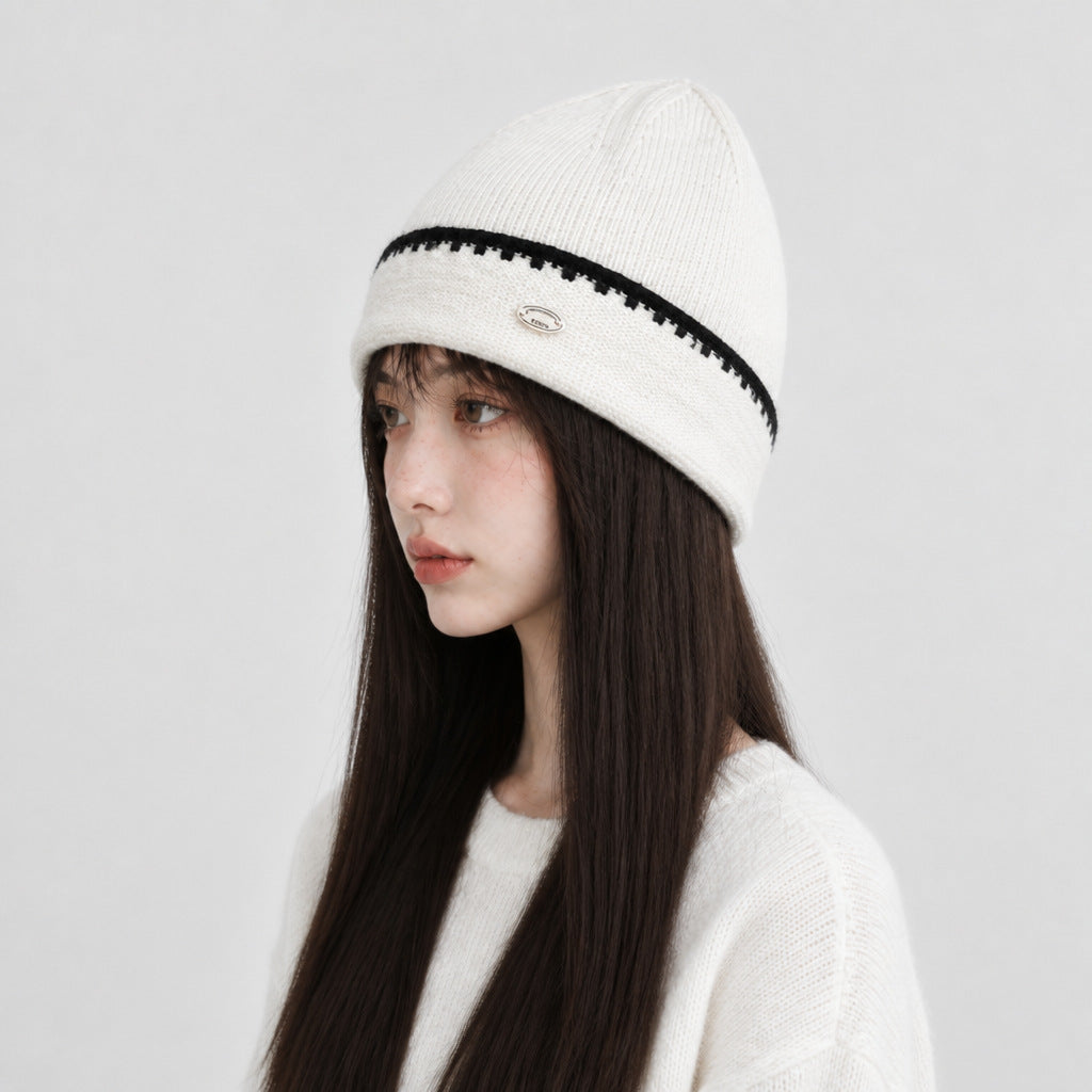 White knit beanie hat with black striped band and small oval logo patch