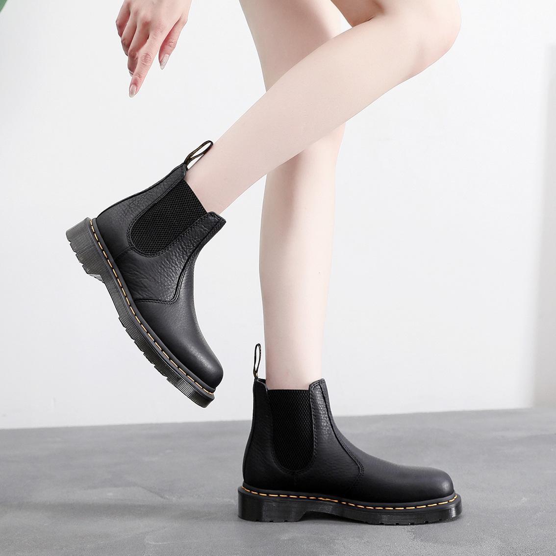Black leather Chelsea boots on model, elastic ankle gore and yellow-stitched sole