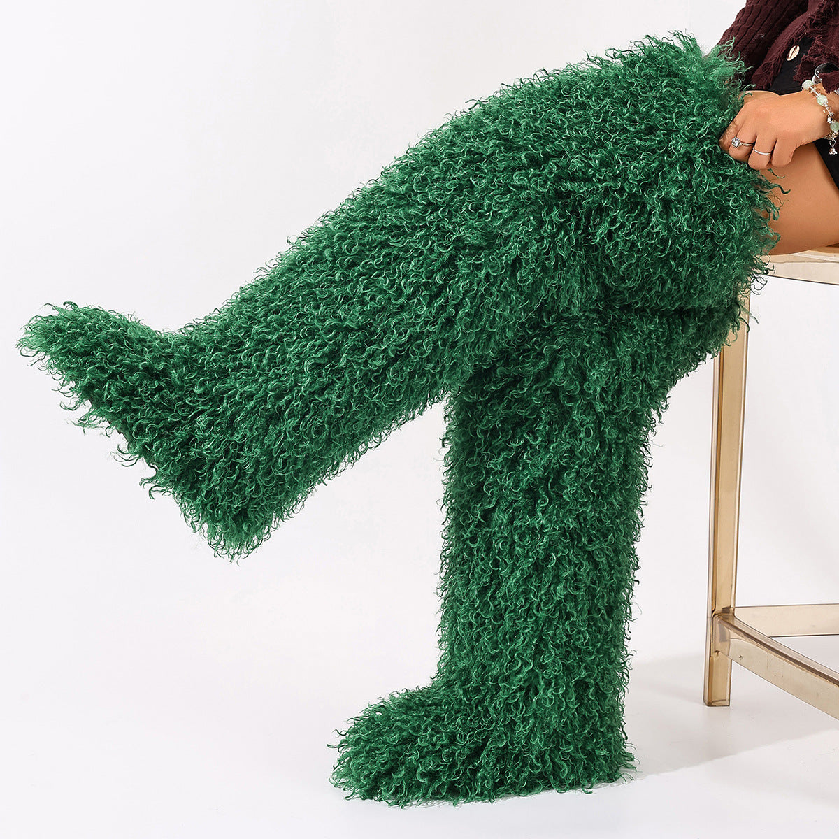 Green faux-fur thigh-high boots with curly pile, shown worn with one leg raised.