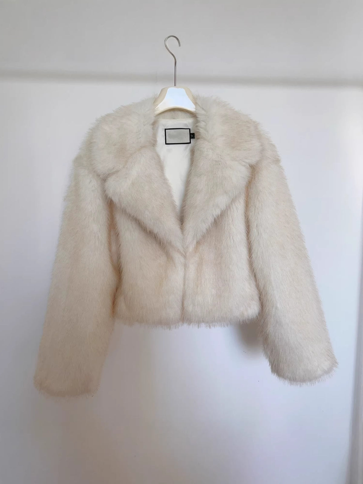 Women's cream faux fur jacket on hanger, pointed lapel V-neck, long sleeves.