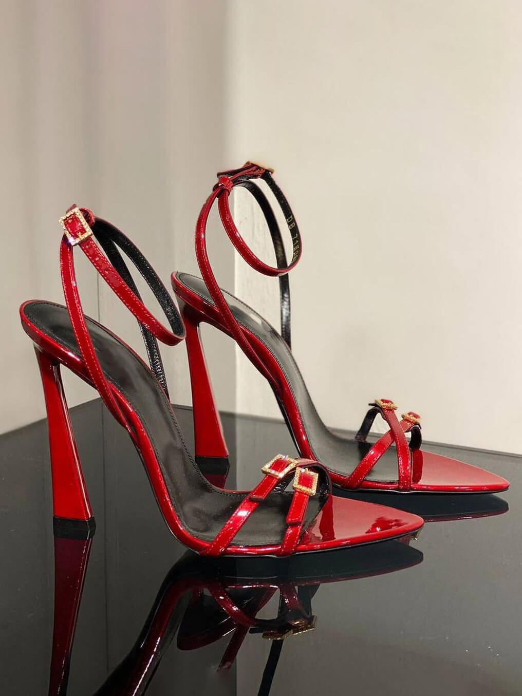 Red patent open-toe stiletto heels with crisscross straps and rhinestone buckle detail