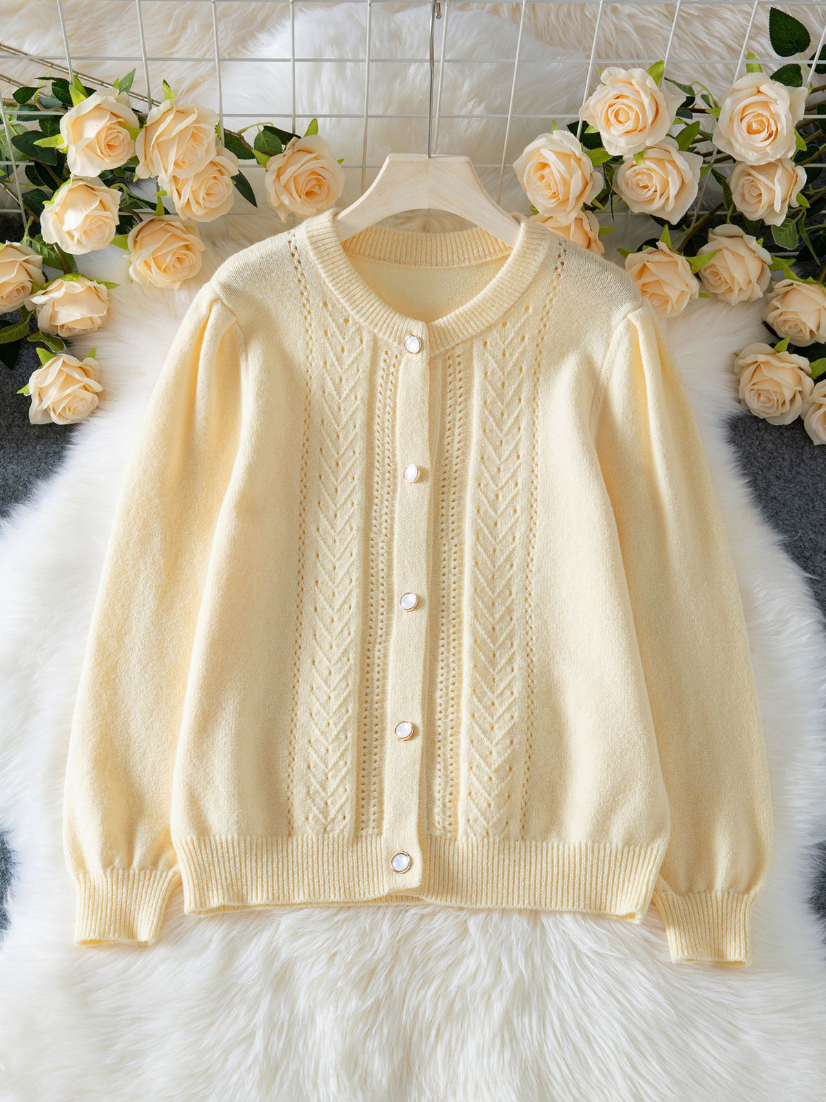 Front view of a cream knit cardigan with openwork panels, buttons, and ribbed edges