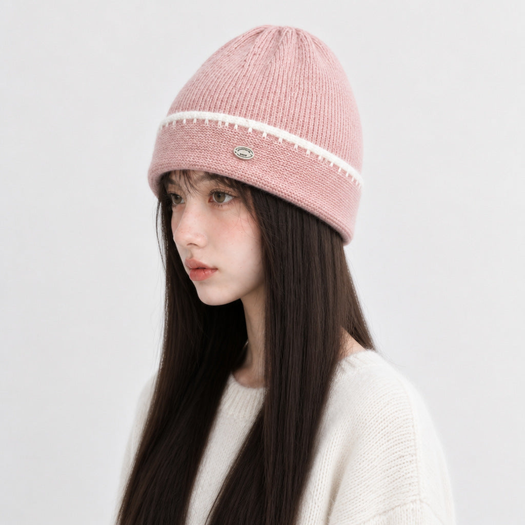 Pink knit beanie hat with white striped band and small oval logo patch