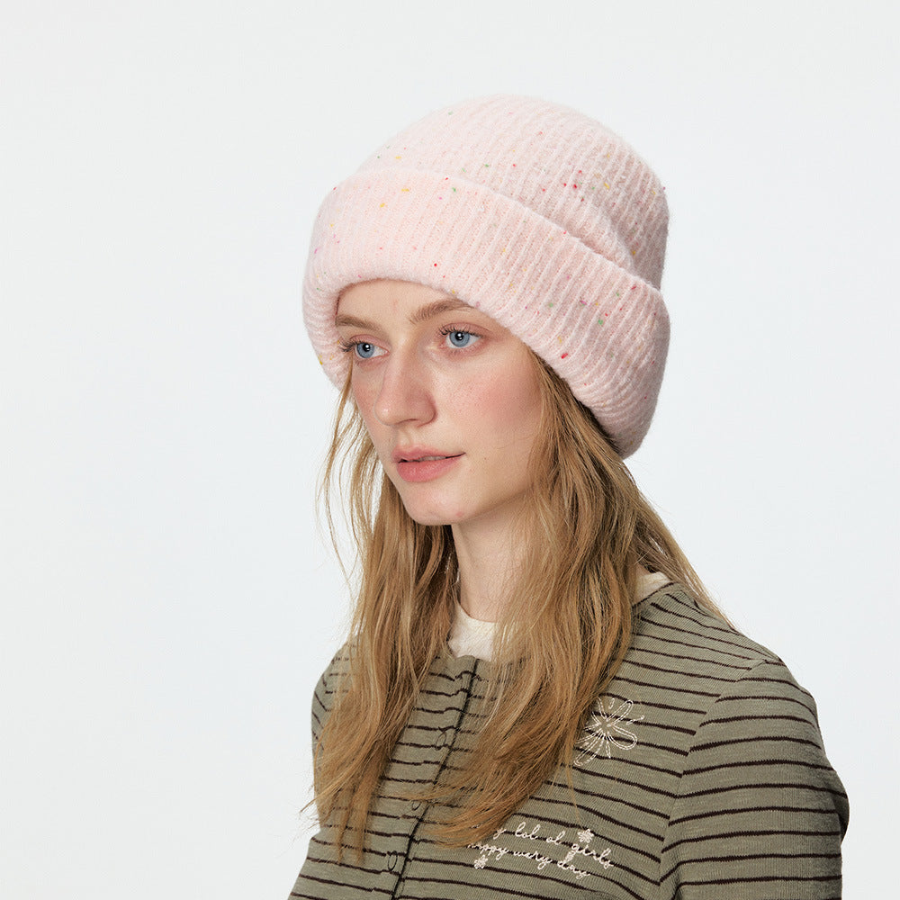 Pale pink speckled rib-knit beanie with a wide folded cuff, modeled.