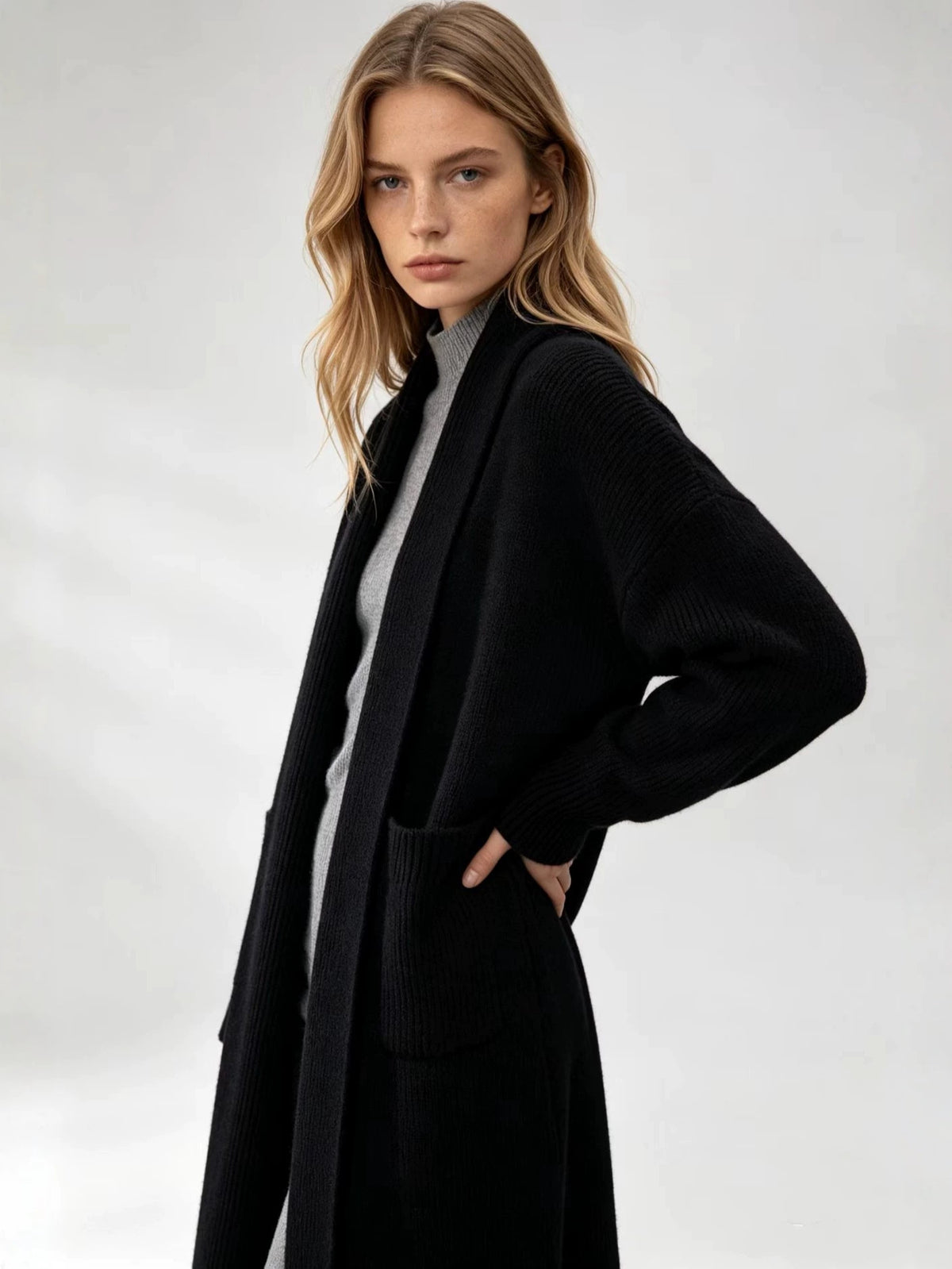 Black knitted cardigan sweater with open front, long sleeves, and side patch pockets