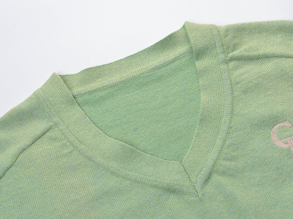 Green knitted V-neck sweater close-up showing ribbed neckline and small chest logo