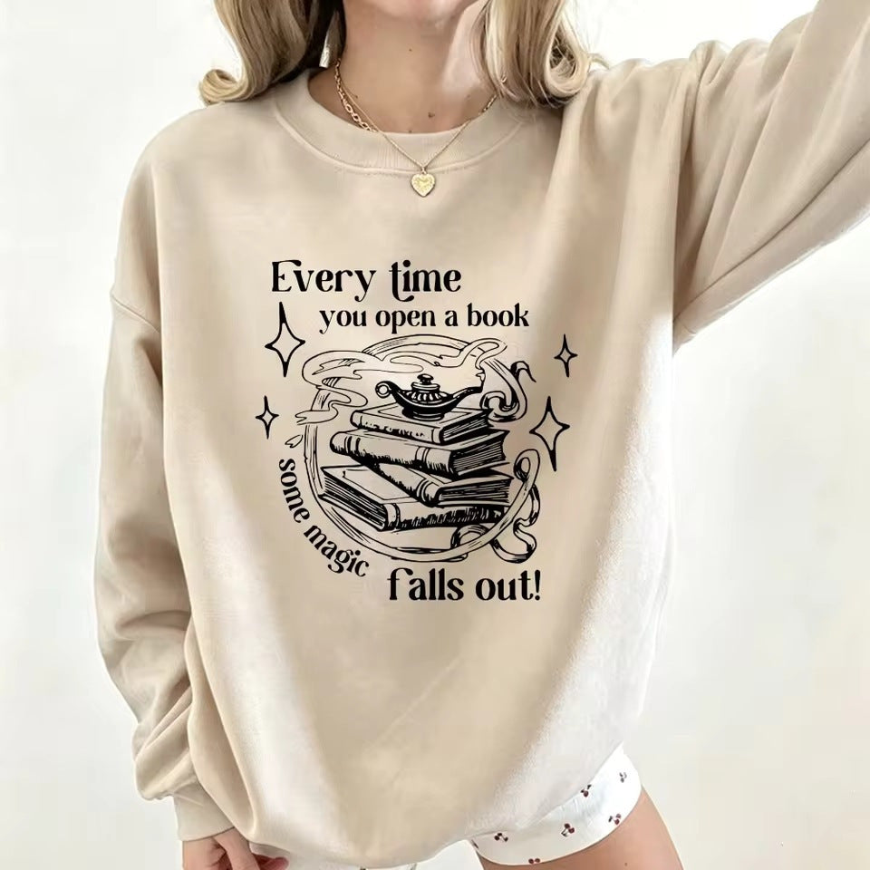 Beige crewneck sweatshirt with open-book magic graphic and starry text, long sleeves.