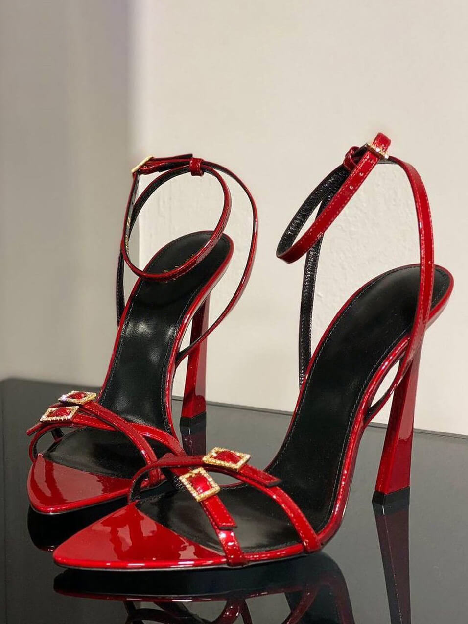 Red patent strappy stiletto heels with open toe and rhinestone buckle, side view