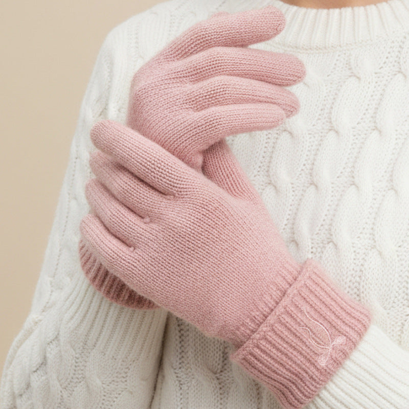 Pink knitted gloves worn on hands, with ribbed cuffs and a small bow detail.