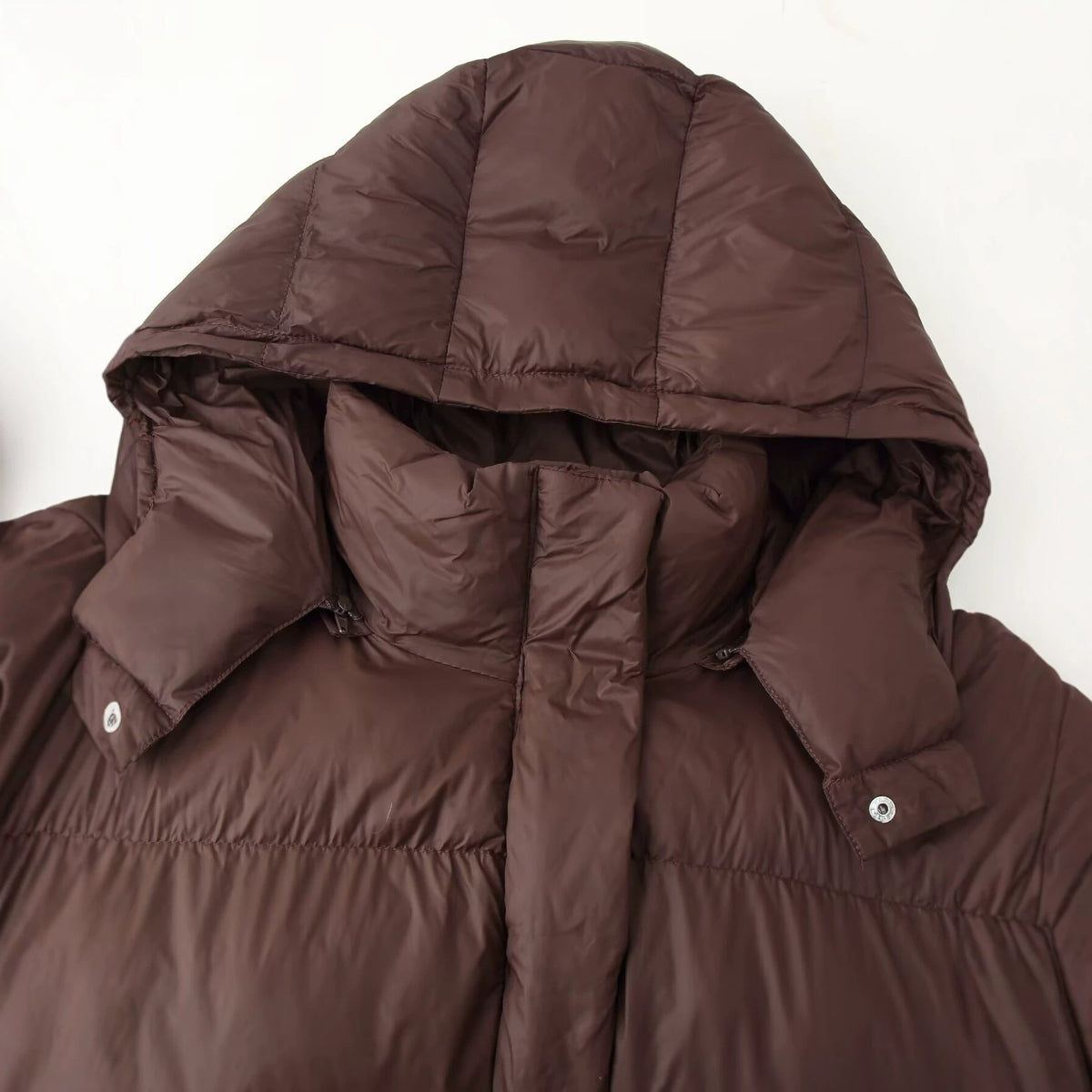 Brown quilted puffer jacket close-up: hood edge, snap buttons, and stitched panels