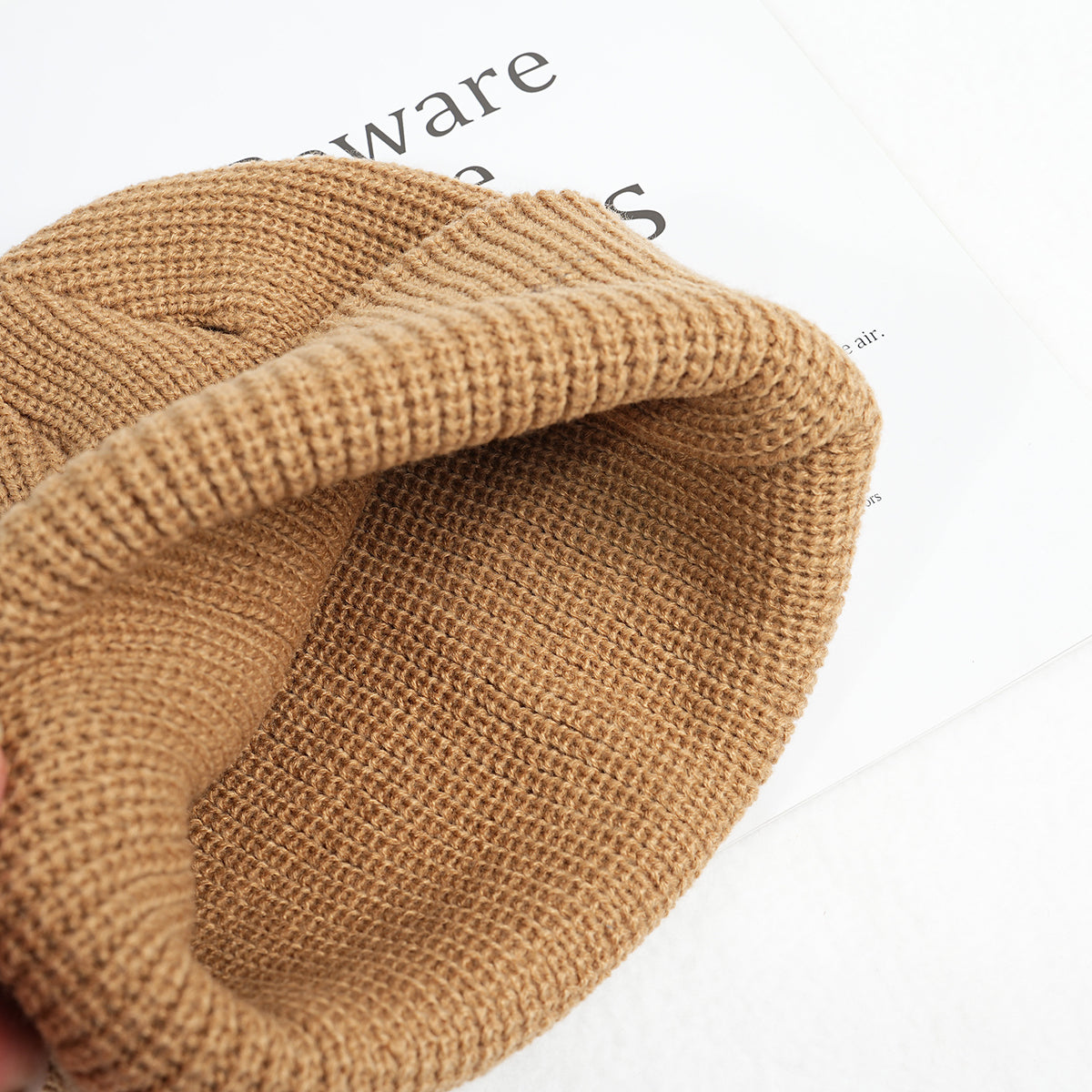 Tan knitted beanie hat with folded brim and visible textured stitch pattern