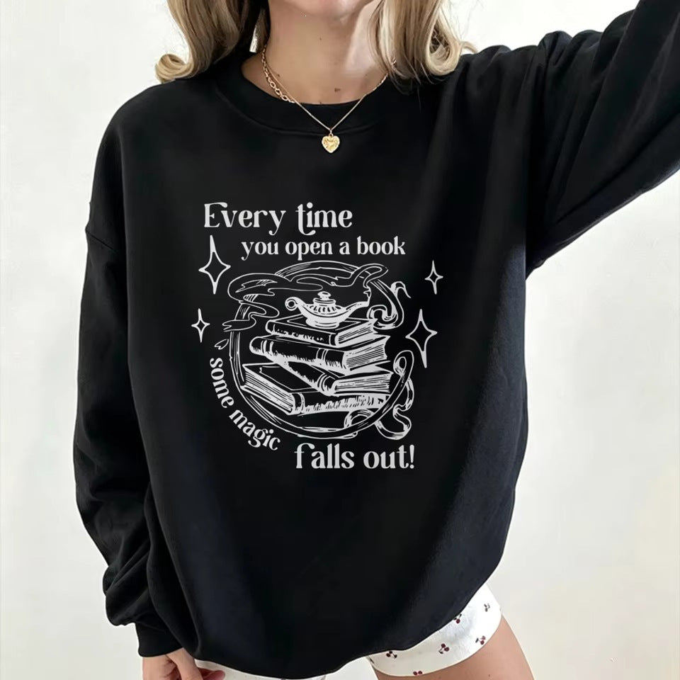 Black crewneck sweatshirt with open-book magic graphic and starry text, long sleeves.