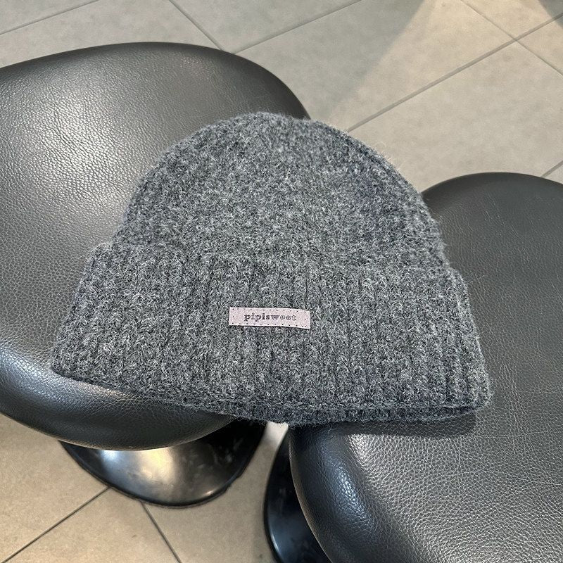 Dark gray heather knit beanie hat with ribbed brim and pipiswoot logo patch