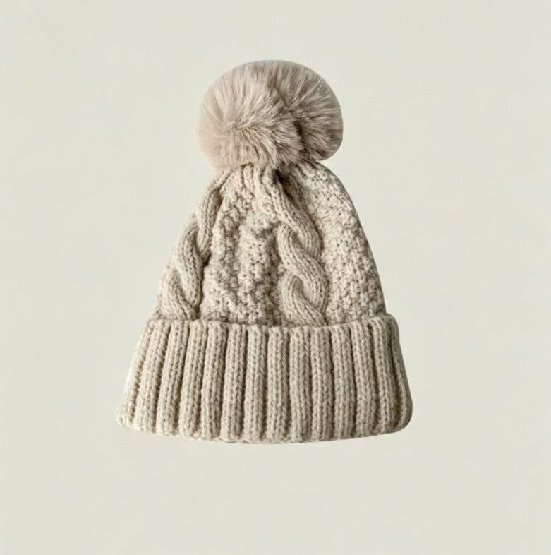 Light beige cable-knit winter hat with ribbed cuff and fluffy pom-pom