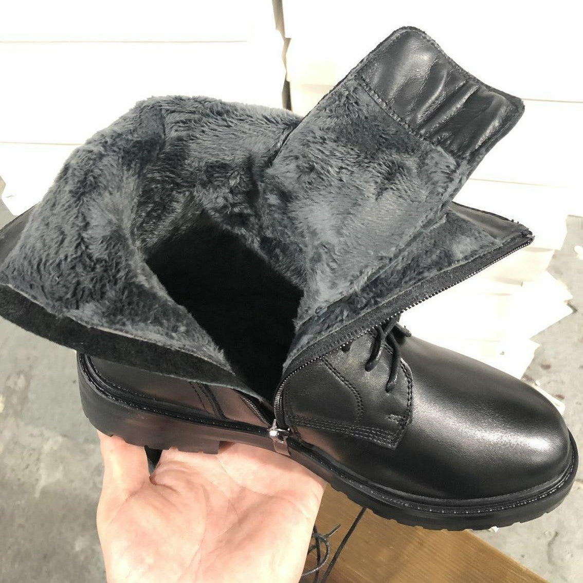 Women’s black mid-calf boots held in hand, lace-up front and plush lining