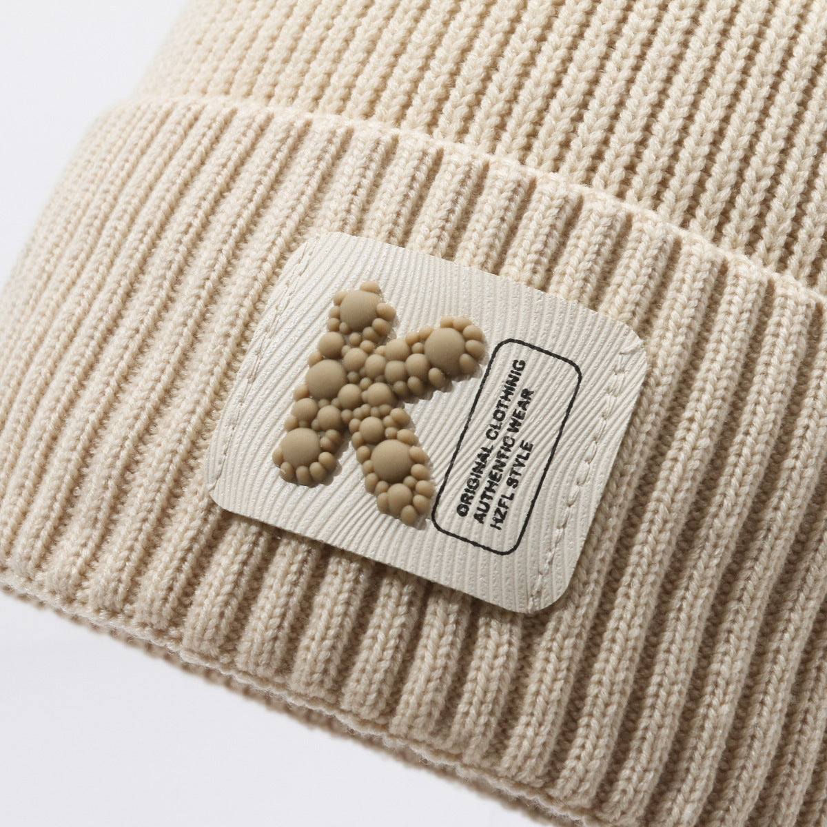 Close-up of khaki rib-knit beanie cuff with fabric brand label patch