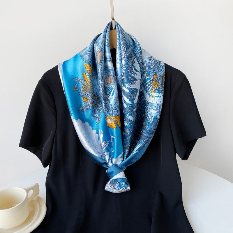 Blue silk square scarf with tropical leaf and bird print, knotted on a black shirt.