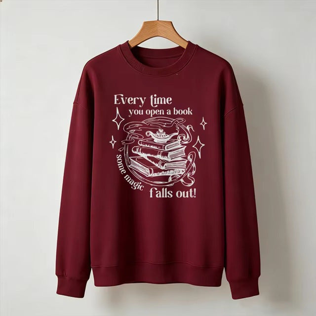 Wine red crewneck sweatshirt with open-book magic graphic and starry text, long sleeves.
