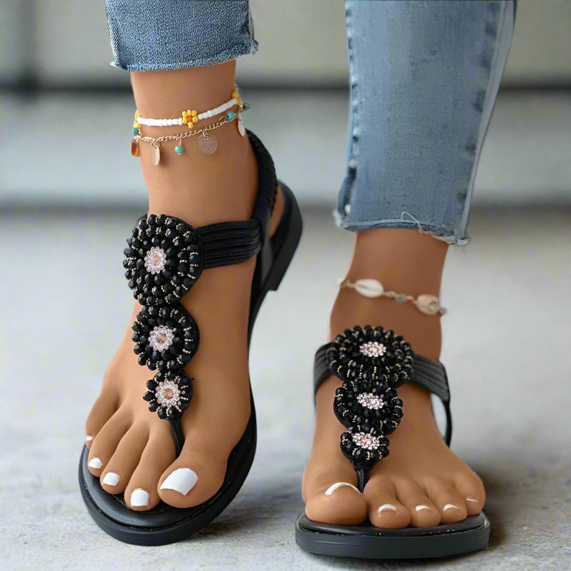 Black flat thong sandals with woven ankle strap and pink-and-silver beaded medallions