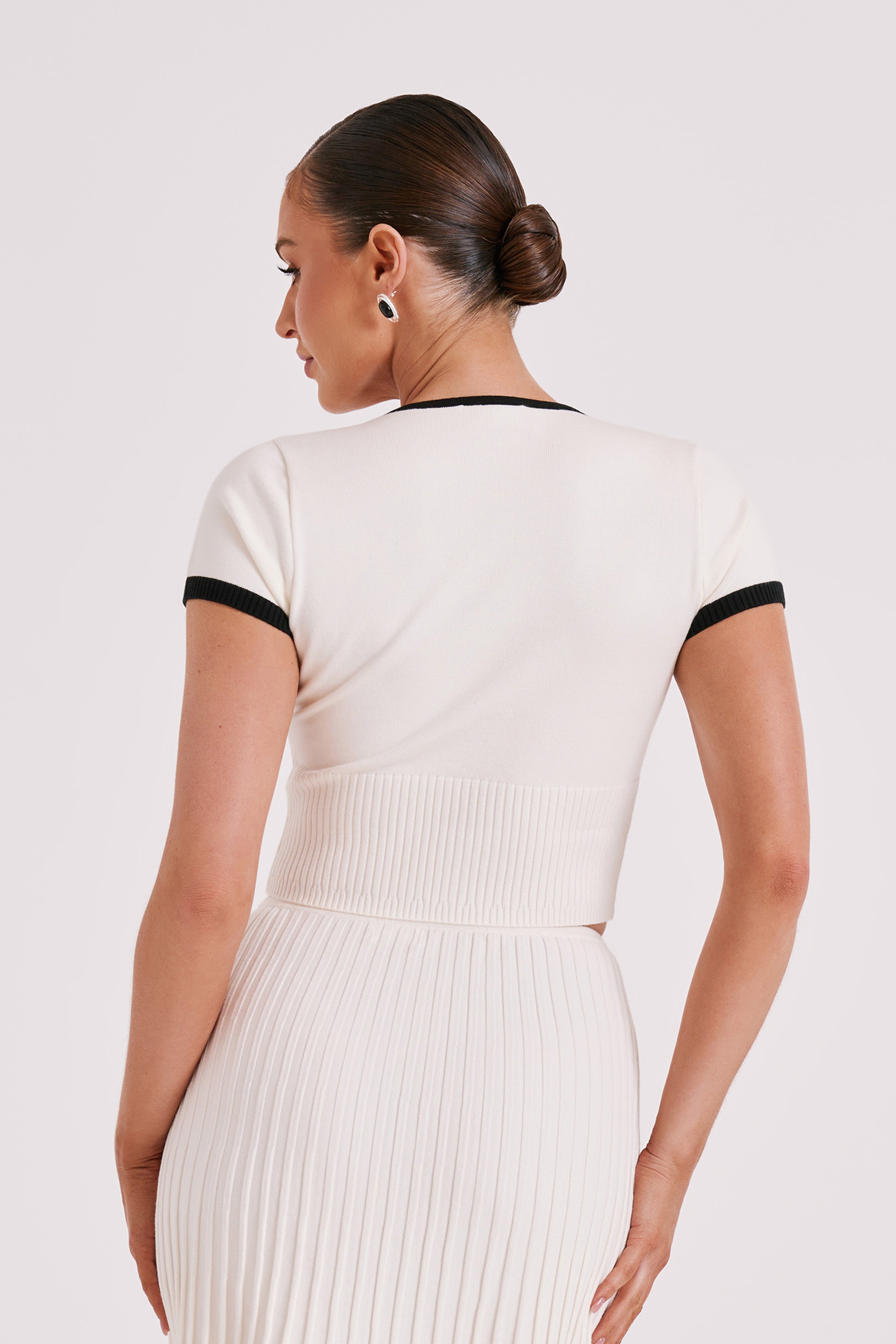 Back view of white ribbed crop top and pleated midi skirt with black-trim edges.