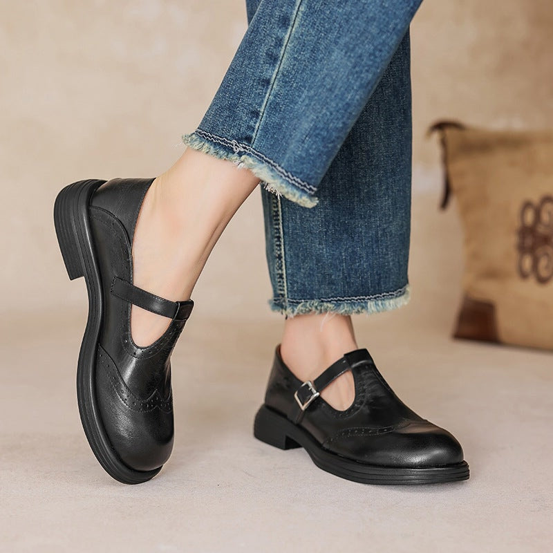 Black leather Mary Jane flat with T-strap buckle and brogue detail, worn with jeans.