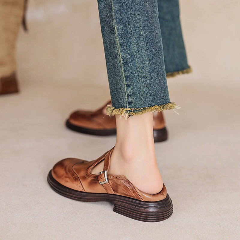 Brown leather Mary Jane flat with T-strap buckle and textured lug sole, worn with jeans.
