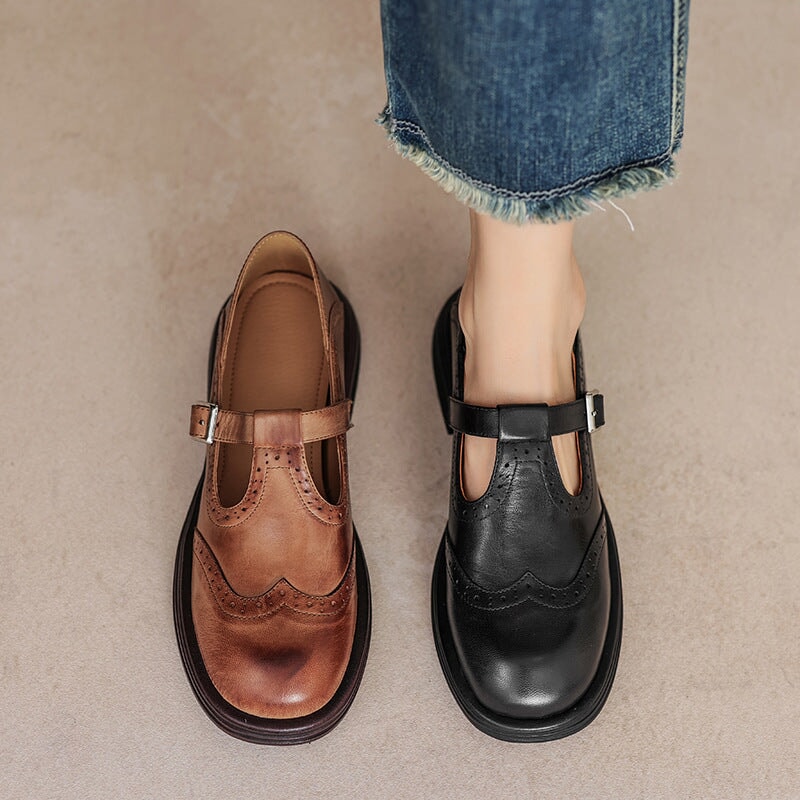 Brown and black leather Mary Jane flats with brogue perforations and T-strap buckles.
