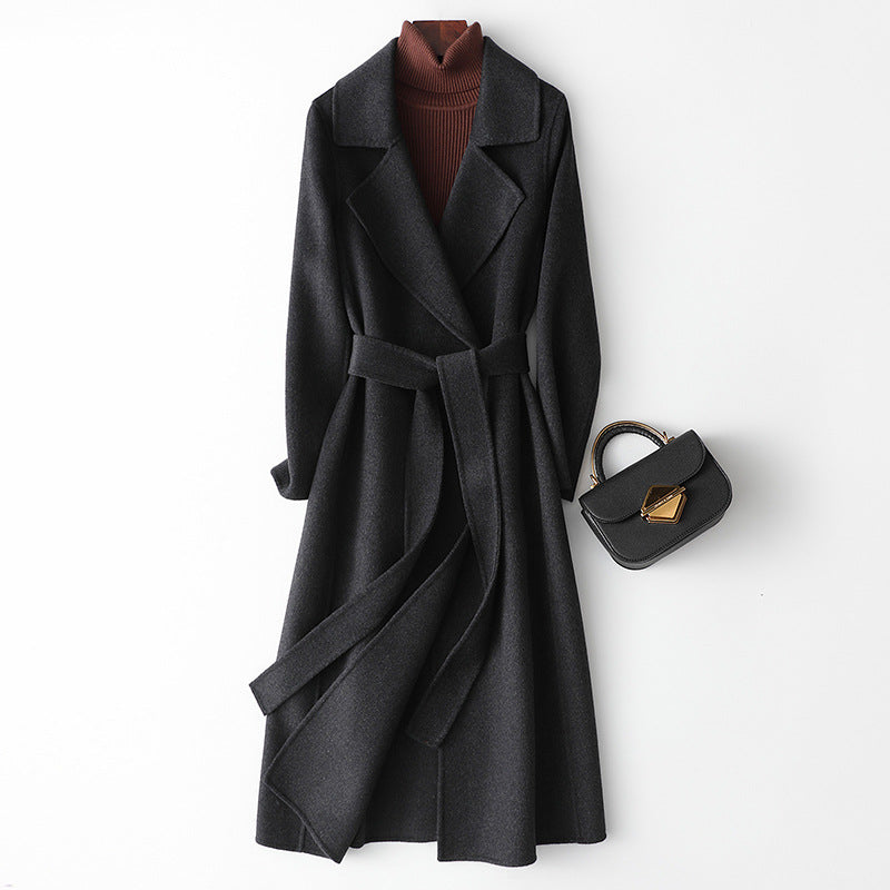 Women’s black long wool-cashmere coat with notched lapels and tied waist belt.